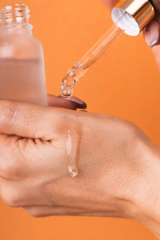 Hand applying face serum drops from dropper bottle showing proper skincare application technique