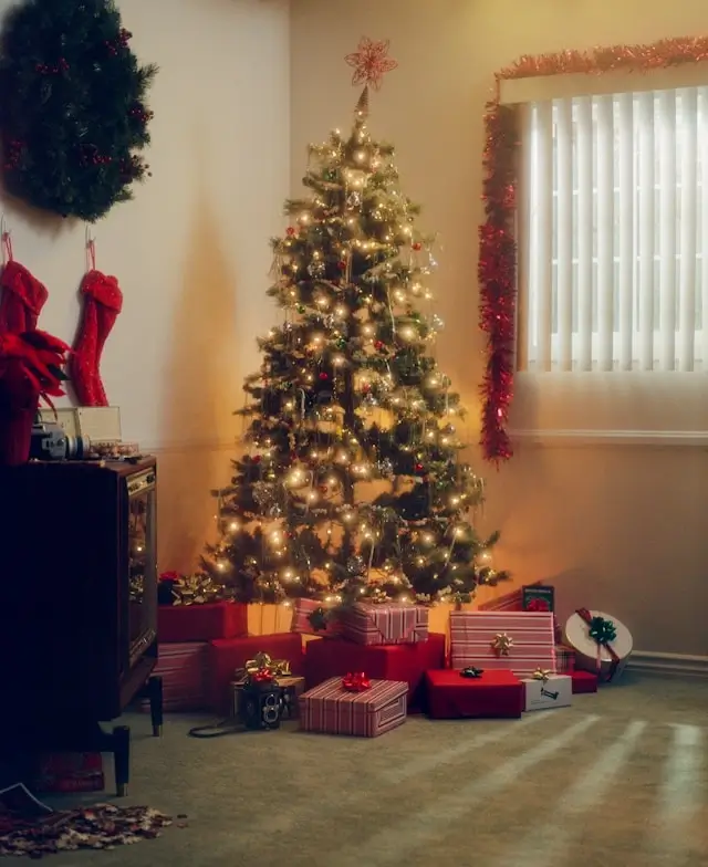 Illuminated Christmas tree with presents underneath in cozy living room with red stockings and holiday decorations