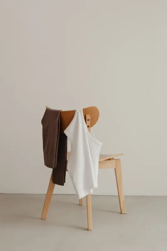 Dark brown cotton leggings and white tank top draped over wooden chair in minimalist neutral room