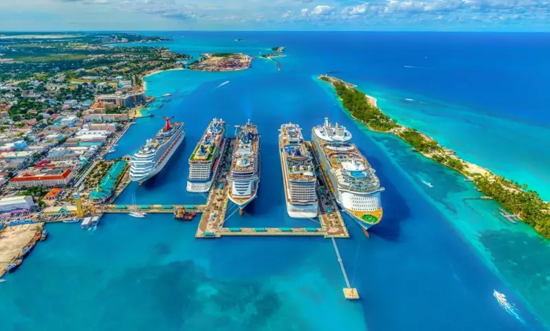 Aerial view of large ocean cruise ships docked at tropical port with turquoise waters and green island in background