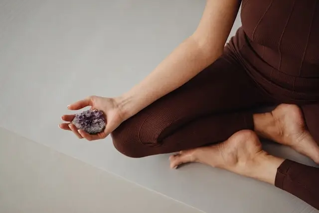Person in meditation pose holding purple amethyst crystal in palm, demonstrating crystal clarity and natural color for authentic gemstone identification