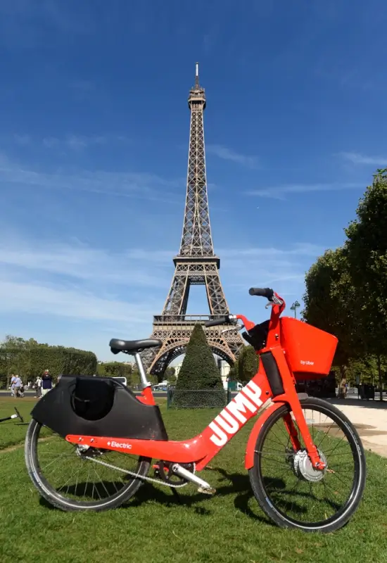 Red electric bike parked on grass with iconic Eiffel Tower in background on clear summer day in Paris, France