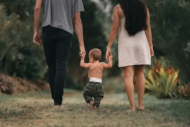 Parents walking hand-in-hand with toddler on outdoor path during family travel adventure