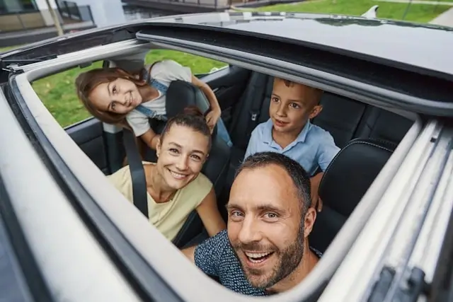Happy family of four smiling from inside car with sunroof open during road trip vacation