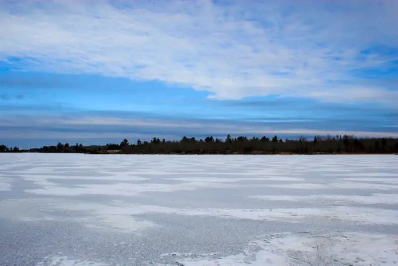 Frozen Crane Lake in winter with snow-covered ice and tree line under blue sky in northern Minnesota