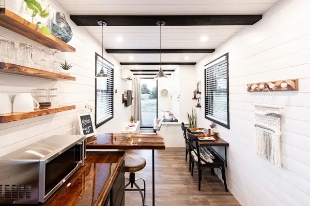 Interior of garden pods showing modern compact kitchen with wooden shelving, dining area, and white shiplap walls for comfortable year-round staycation use