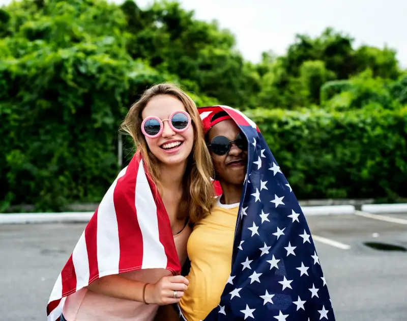 Two diverse women celebrating with American flag representing community and lifestyle for people moving to USA