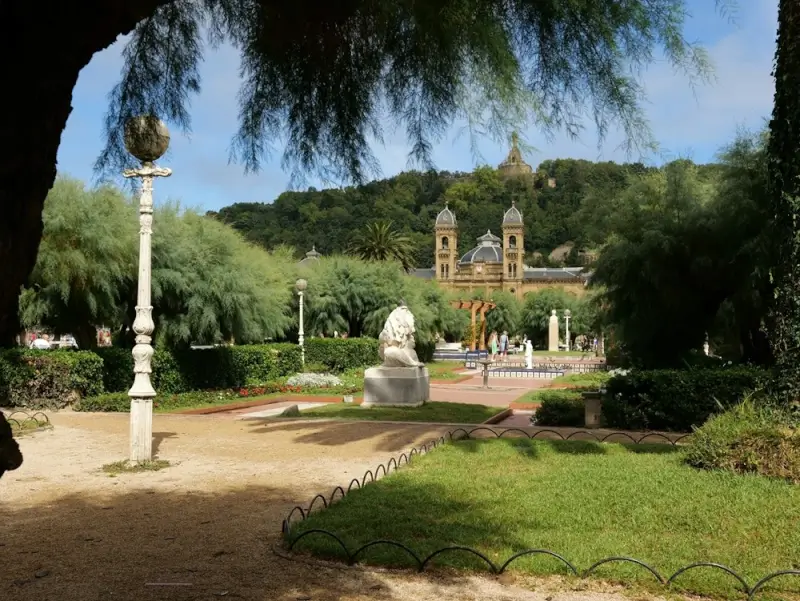 Miramar Palace gardens in San Sebastian with manicured lawns, ornate lamp posts, and the Santa Maria del Coro Cathedral in the background, a scenic stop for cyclists touring the coastal promenade