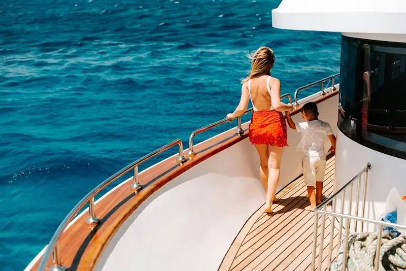 Woman and child standing on luxury cruise ship deck overlooking deep blue ocean waters on sunny day