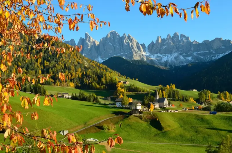 Italian Dolomites autumn landscape with colorful leaves, traditional Alpine village, and dramatic mountain peaks