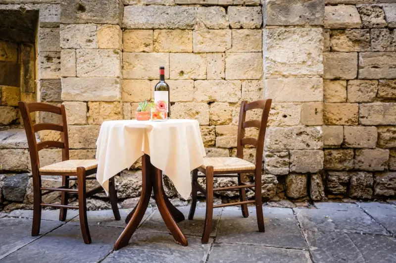 Rustic Italian restaurant table with wine and traditional chairs on historic cobblestone alley