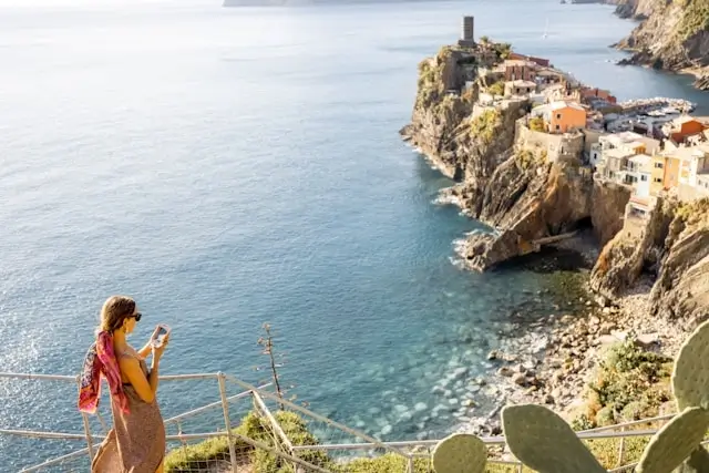 Tourist photographing Vernazza village from hiking trail in Cinque Terre Italy - scenic coastal viewpoint for Instagram photos