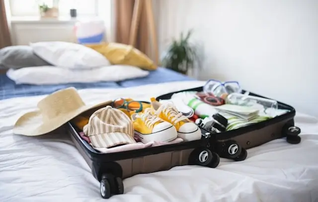 Open suitcase packed with summer vacation essentials including bikinis, straw hat and sunglasses for Ibiza trip