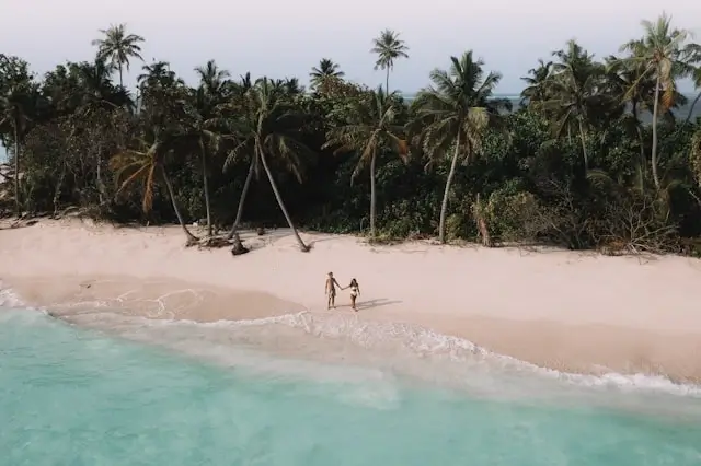 Two people walking on a secluded Maldives beach with turquoise water and palm trees during shoulder season