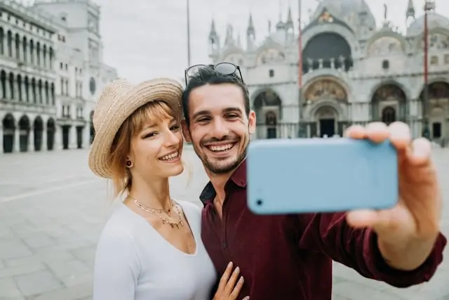 Happy couple taking a selfie in front of St. Mark's Basilica in Venice, Italy, capturing their travel experience on smartphone