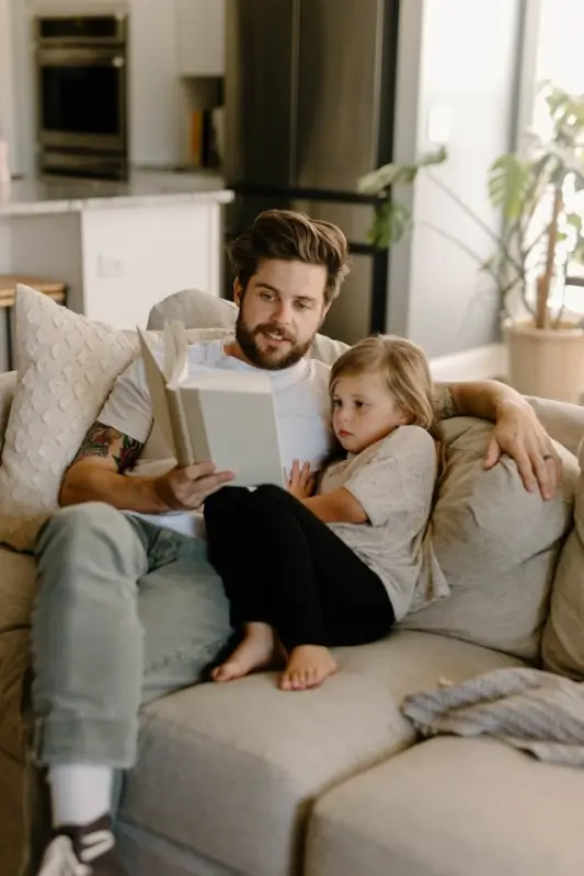 Father and daughter sharing a cozy reading moment together on living room couch