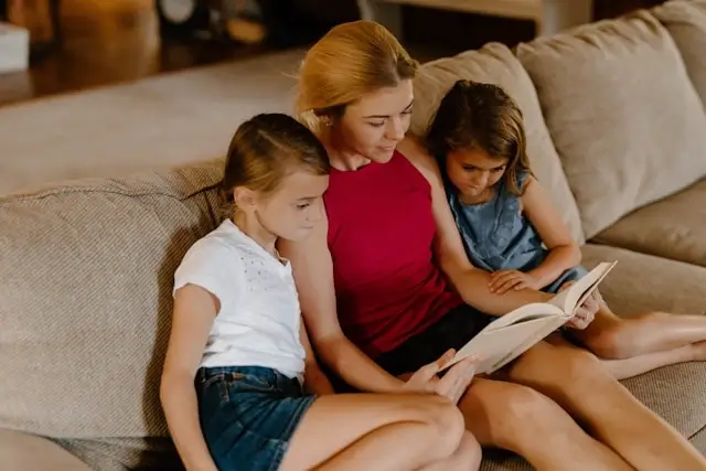 Mother reading aloud to two young daughters during quality family time on couch