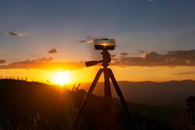 Smartphone mounted on tripod recording a golden sunset over mountains, representing travel content creation