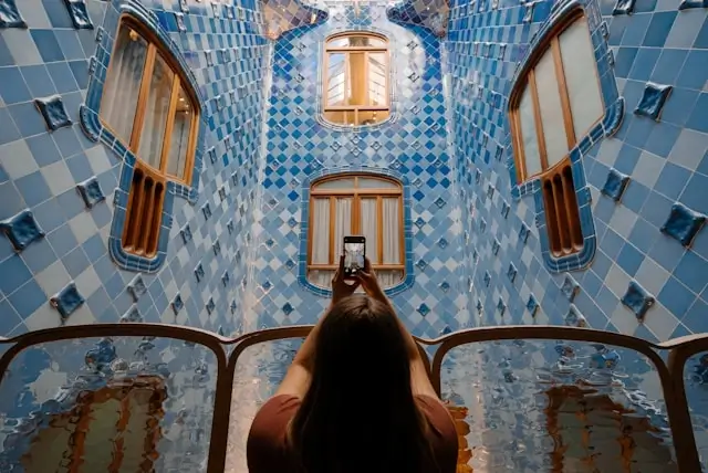 Traveler photographing the ornate blue-tiled courtyard of Casa Batlló in Barcelona with a smartphone from above