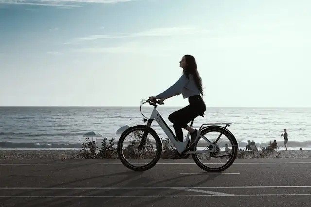 Woman riding white e-bike along scenic beachfront path with ocean view in background
