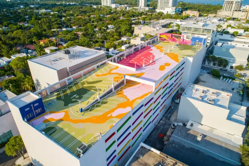 Aerial view of colorful rooftop basketball courts in Miami with vibrant pink, orange, yellow, and green abstract patterns painted across multiple levels of a parking garage structure