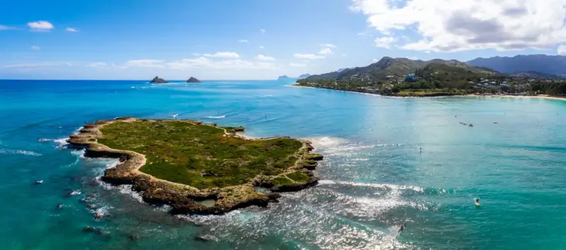 Aerial view of Mokulua Islands off Kailua Beach with turquoise ocean waters, green vegetation-covered rocky terrain, and Oahu's coastline and mountains in the background