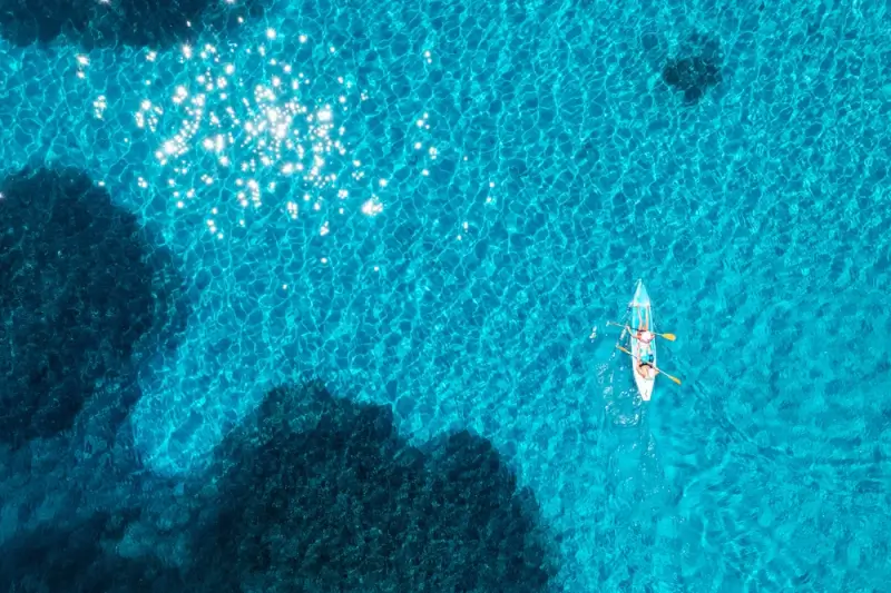 Aerial view of two people kayaking in crystal clear turquoise waters near Mokulua Islands with visible coral reefs and rocky formations below