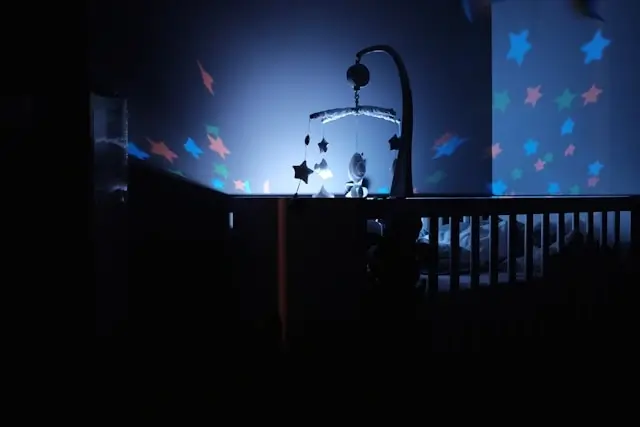 Baby crib in dark nursery with star mobile projecting colorful stars on walls creating calming sleep environment