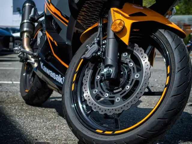 Close-up of Kawasaki motorcycle front wheel showing orange and black color scheme with perforated brake disc and caliper