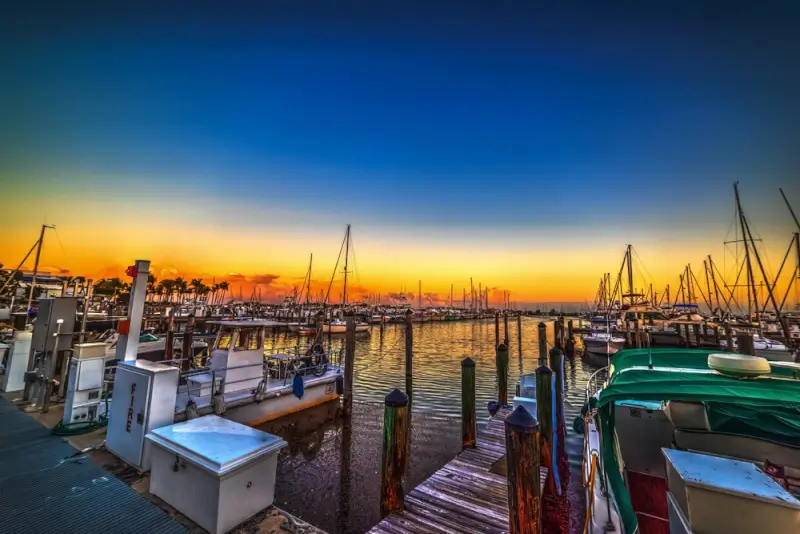 Miami marina at sunset with boats docked along wooden piers, reflecting golden and orange hues on calm water under a vibrant blue and yellow sky