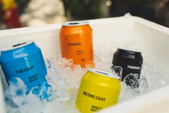 Colorful beverage cans packed in ice inside a white portable cooler, showing properly chilled drinks ready for consumption during a road trip