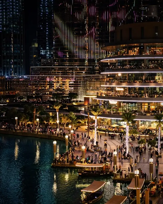 Downtown Dubai waterfront promenade at night with illuminated hotels near Dubai Mall and crowds enjoying The Dubai Fountain area
