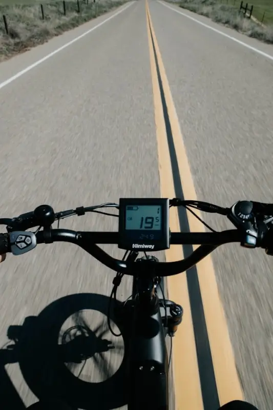 First-person view of e-bike handlebars with digital display showing speed on open rural road