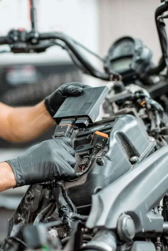 Mechanic's hands in black gloves removing or installing motorcycle battery from under-seat compartment in workshop