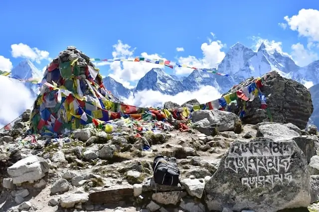 Colorful prayer flags strung across rocky terrain at Everest Base Camp with snow-capped Himalayan peaks and blue sky in the background