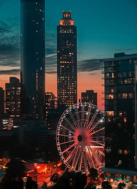 Atlanta skyline at dusk with illuminated Ferris wheel and tall buildings glowing against orange and blue twilight sky showcasing the city's vibrant evening atmosphere for adults