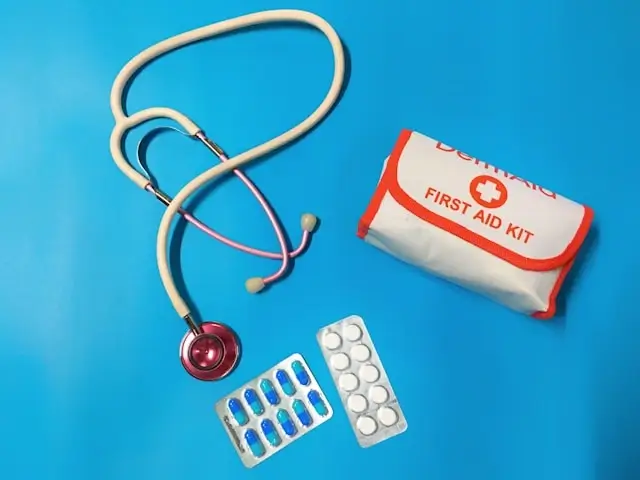 Compact first aid kit with medical supplies including stethoscope, medication blister packs, and white pouch with red cross on blue background