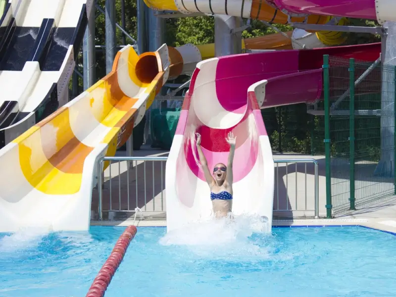 Teenage girl splashing into pool at bottom of colorful water slide at Swiss water park