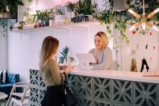Hotel receptionist warmly greeting a loyal guest at a boutique hotel front desk surrounded by plants