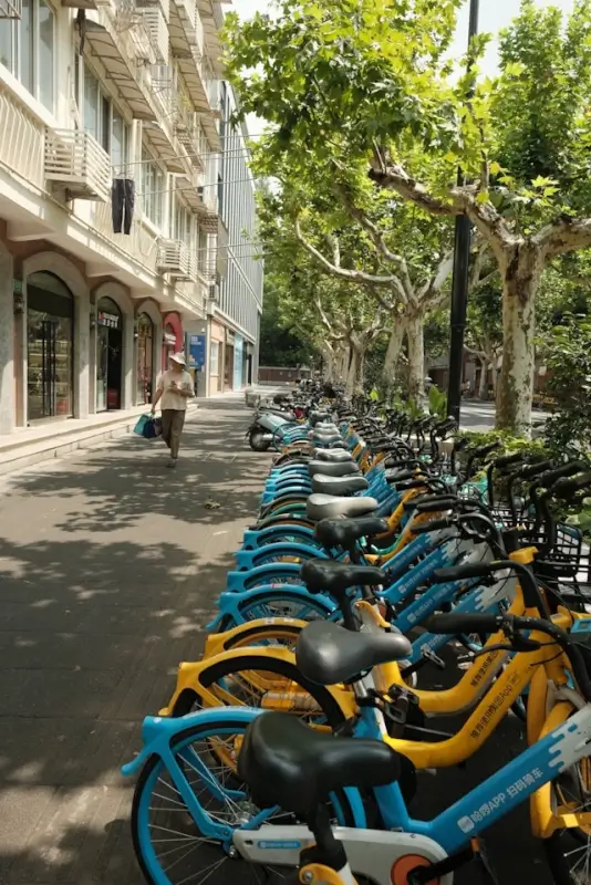 Row of colorful blue and yellow e-bikes parked on tree-lined urban street for bike-sharing