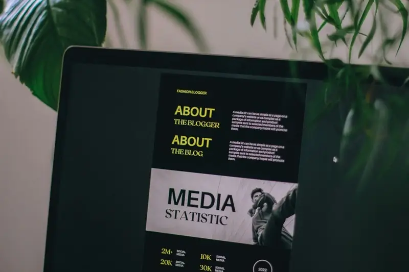 Laptop screen displaying a professional fashion blogger media kit with sections for About the Blogger, About the Blog, and Media Statistics showing social media follower counts on a desk with green plants