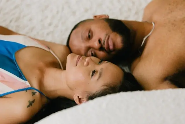 Couple lying close together on bed, woman resting head on man's shoulder, sharing intimate moment