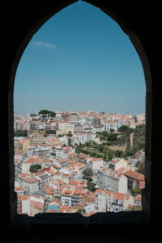 Lisbon cityscape with terracotta rooftops viewed through historic stone archway in Portugal during off-peak winter season