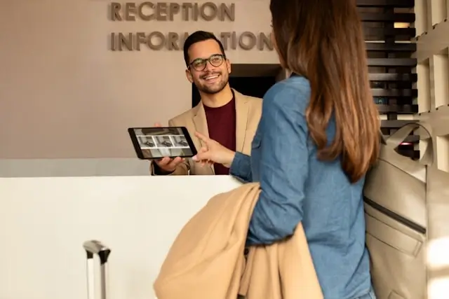 Friendly hotel staff member using a tablet to assist a returning guest at the reception information desk