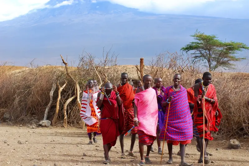 Maasai tribe members in traditional red and colorful shuka garments standing in Amboseli with Mount Kenya in background