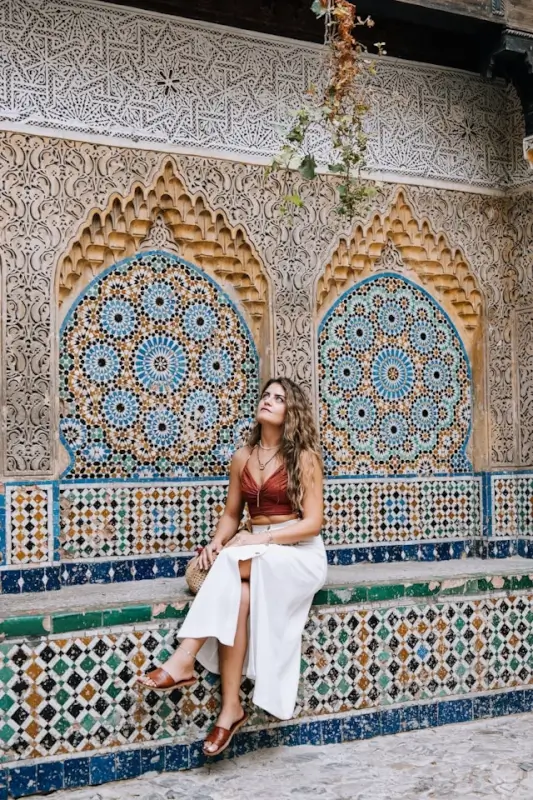 Woman sitting by ornate Moroccan tilework and carved archways in Morocco during affordable winter season