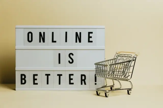 Small shopping cart next to a lightbox sign that reads 'Online Is Better,' symbolizing the convenience of buying products digitally.
