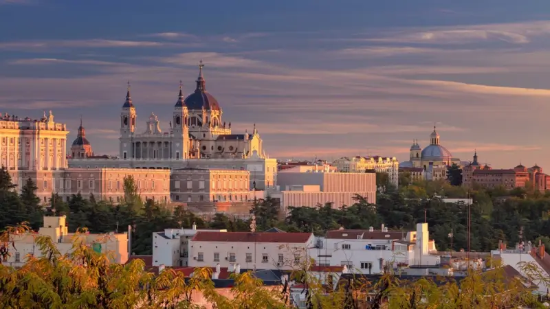 Panoramic sunset view of Madrid skyline featuring Almudena Cathedral and Royal Palace bathed in golden light