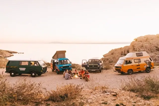Group of travelers taking a scenic break with vans parked by the coast during a road trip adventure
