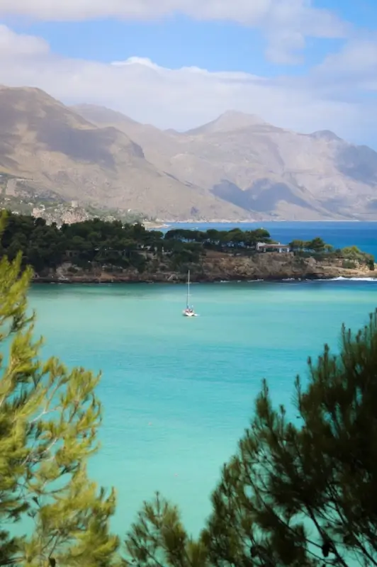 Turquoise waters and sailboat at scenic Sicilian coastline with mountains in background